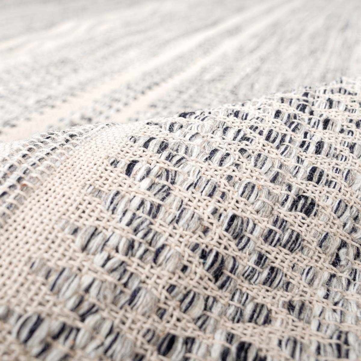 Close-up of the hand-woven Arabi Wool Area Rug, showing its black, gray, and light beige pattern and texture. Fold