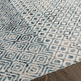 Close-up of the Askeaton Washable Area Rug. Features a geometric diamond pattern in blue, gray, and light gray. Texture