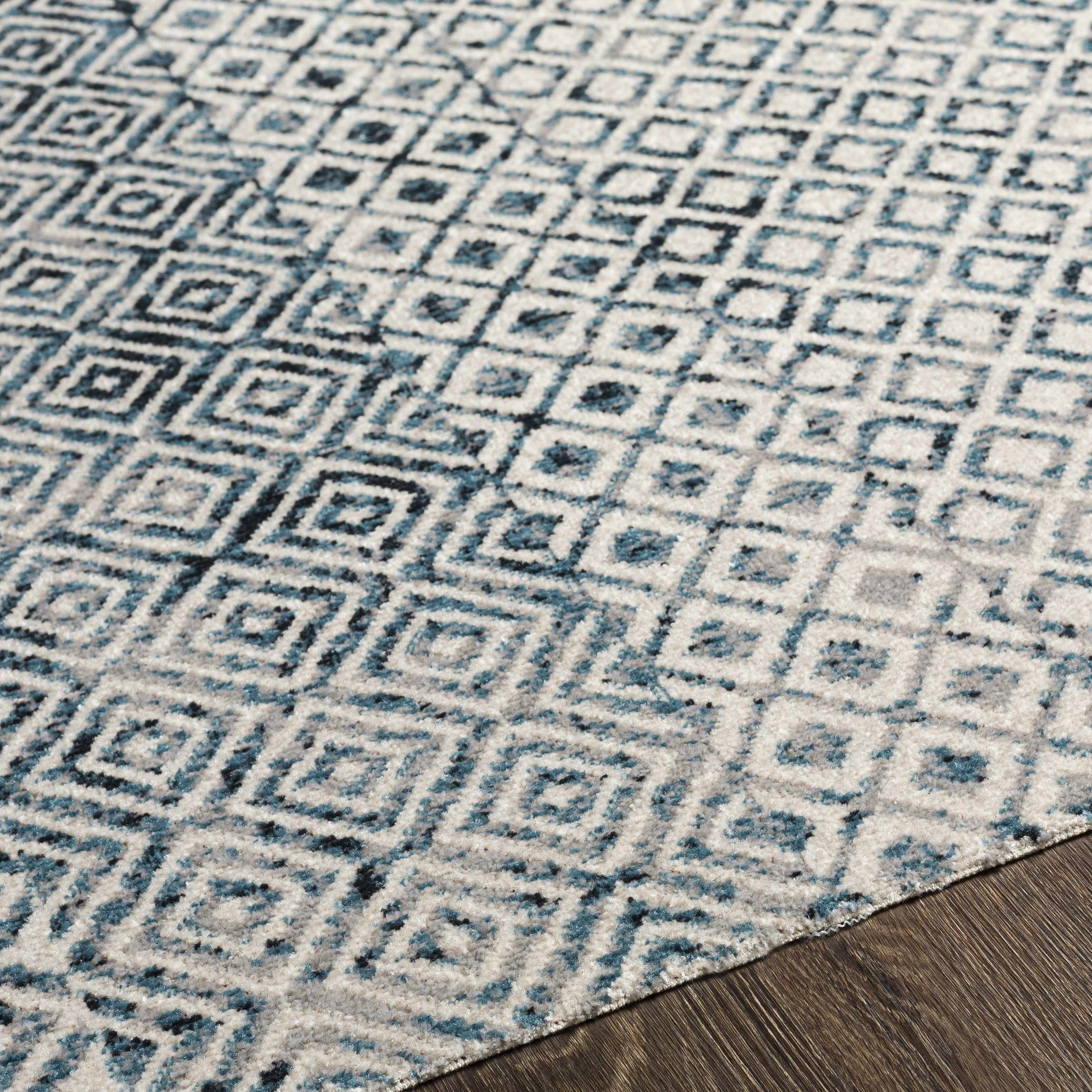 Close-up of the Askeaton Washable Area Rug. Features a geometric diamond pattern in blue, gray, and light gray. Texture
