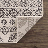Close-up of the Warroad Area Rug showing a charcoal and light beige floral pattern and the rug's backing. Fold