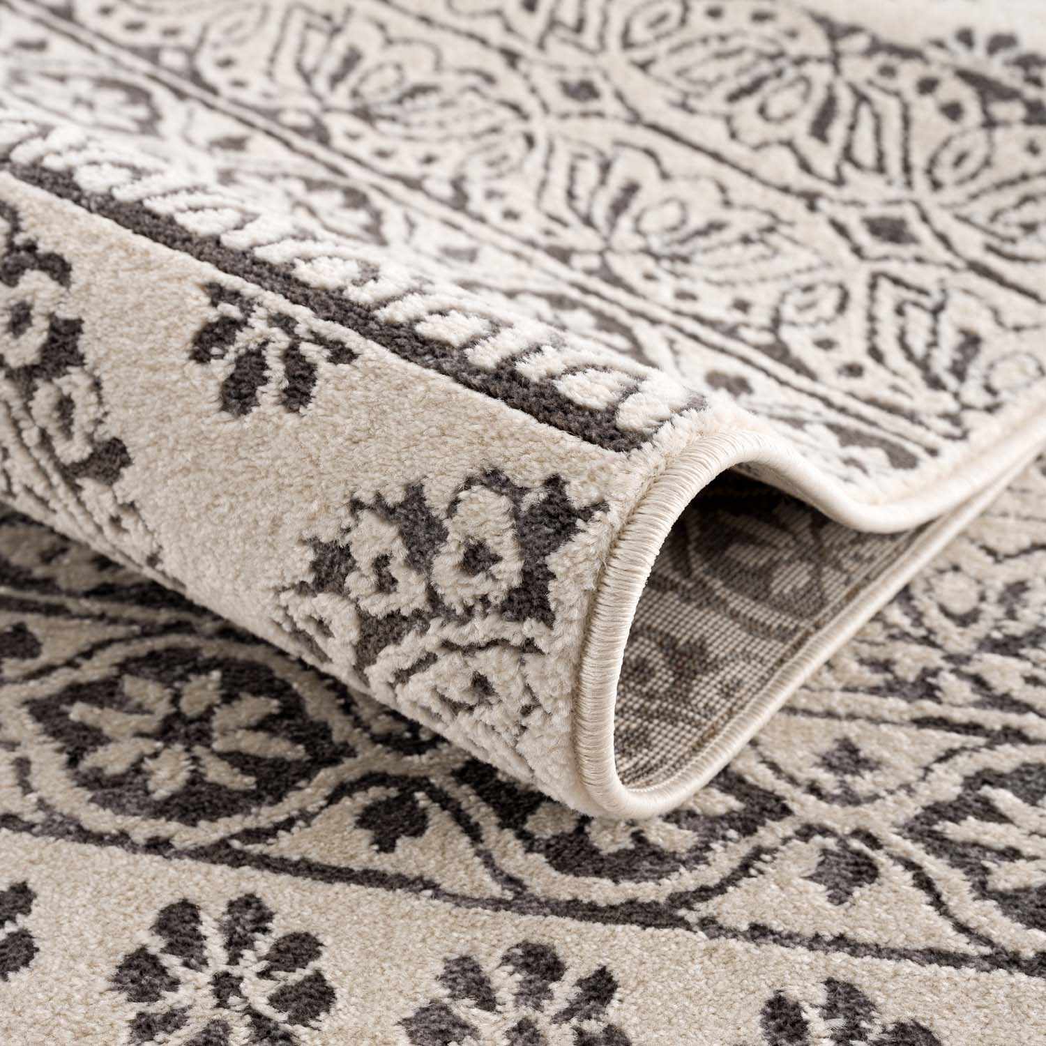 Close-up of the Warroad Area Rug showing its charcoal and beige floral pattern and soft, textured weave. Fold