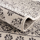 Close-up of the Warroad Area Rug showing its charcoal and beige floral pattern and soft, textured weave. Fold