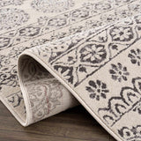 Close-up of the Warroad Area Rug. Beige rug with a charcoal, gray, and light beige traditional floral pattern. Fold