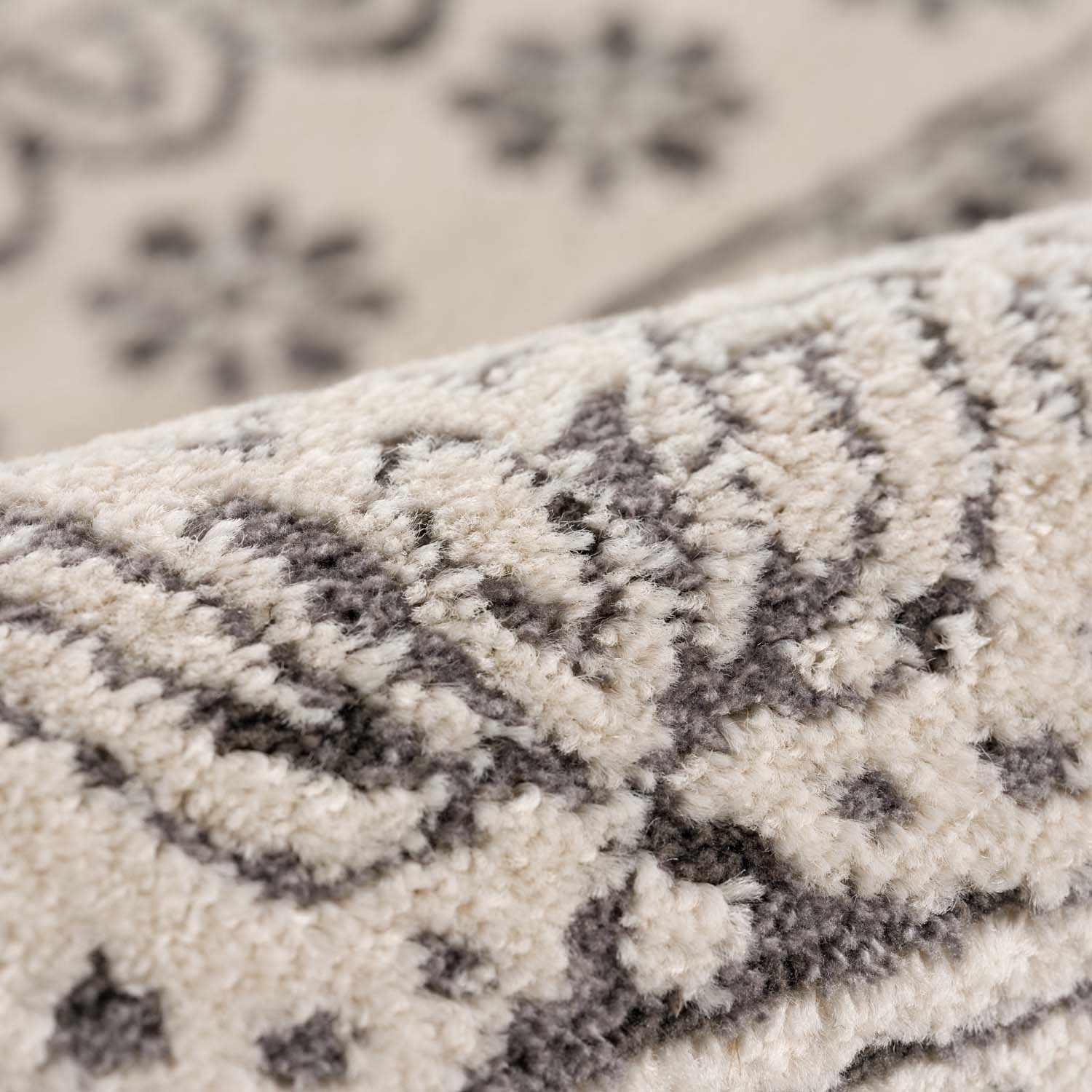 Close-up of the Warroad Area Rug showing its light beige base and charcoal gray bohemian pattern and plush, textured pile. Fold