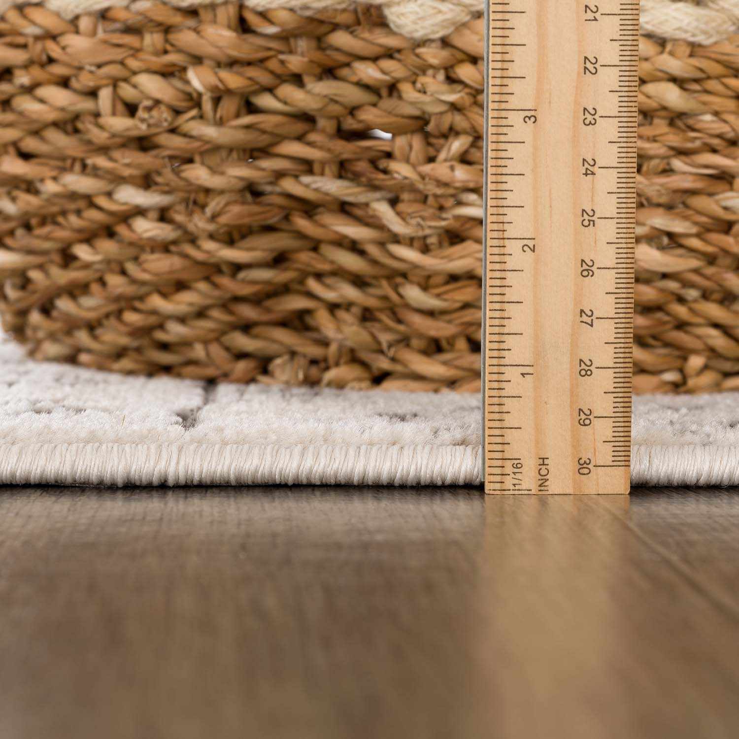 Close-up of the Warroad Area Rug showing pile height with a ruler and woven basket. Light beige color. Pile