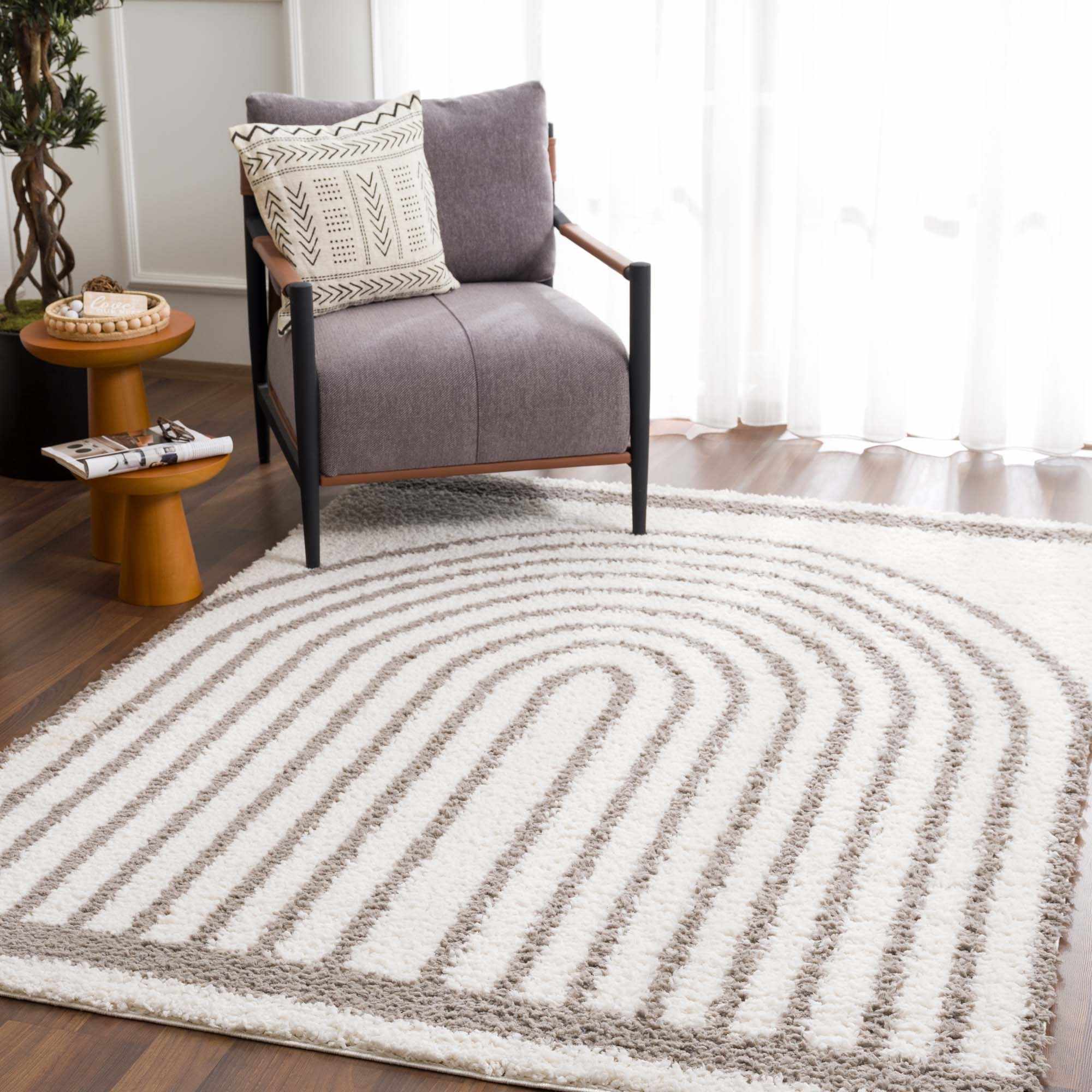 Living room scene with a gray chair on a Jola Taupe Area Rug with a geometric pattern. Modern, neutral tones. Roomscene-Rectangle
