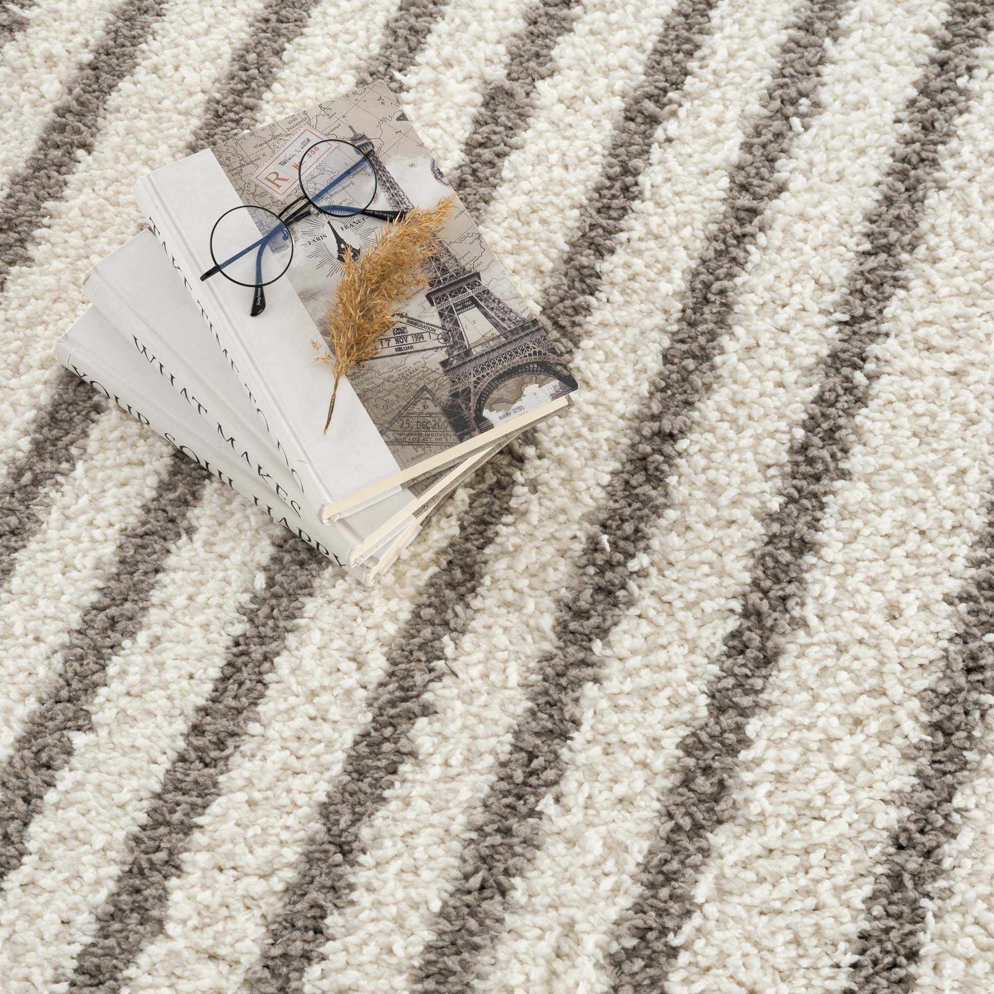 Close-up of the plush Jola Taupe Area Rug with a striped beige and gray geometric pattern and soft, shaggy texture. Styleshot