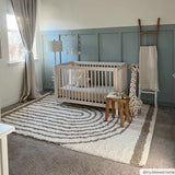 Nursery scene with a beige crib on a Jola Beige Area Rug with a geometric swirl pattern. Blue accent wall. Roomscene-Rectangle