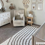 Nursery scene with a white glider chair and striped Jola Beige Area Rug on gray carpet. Roomscene-Rectangle