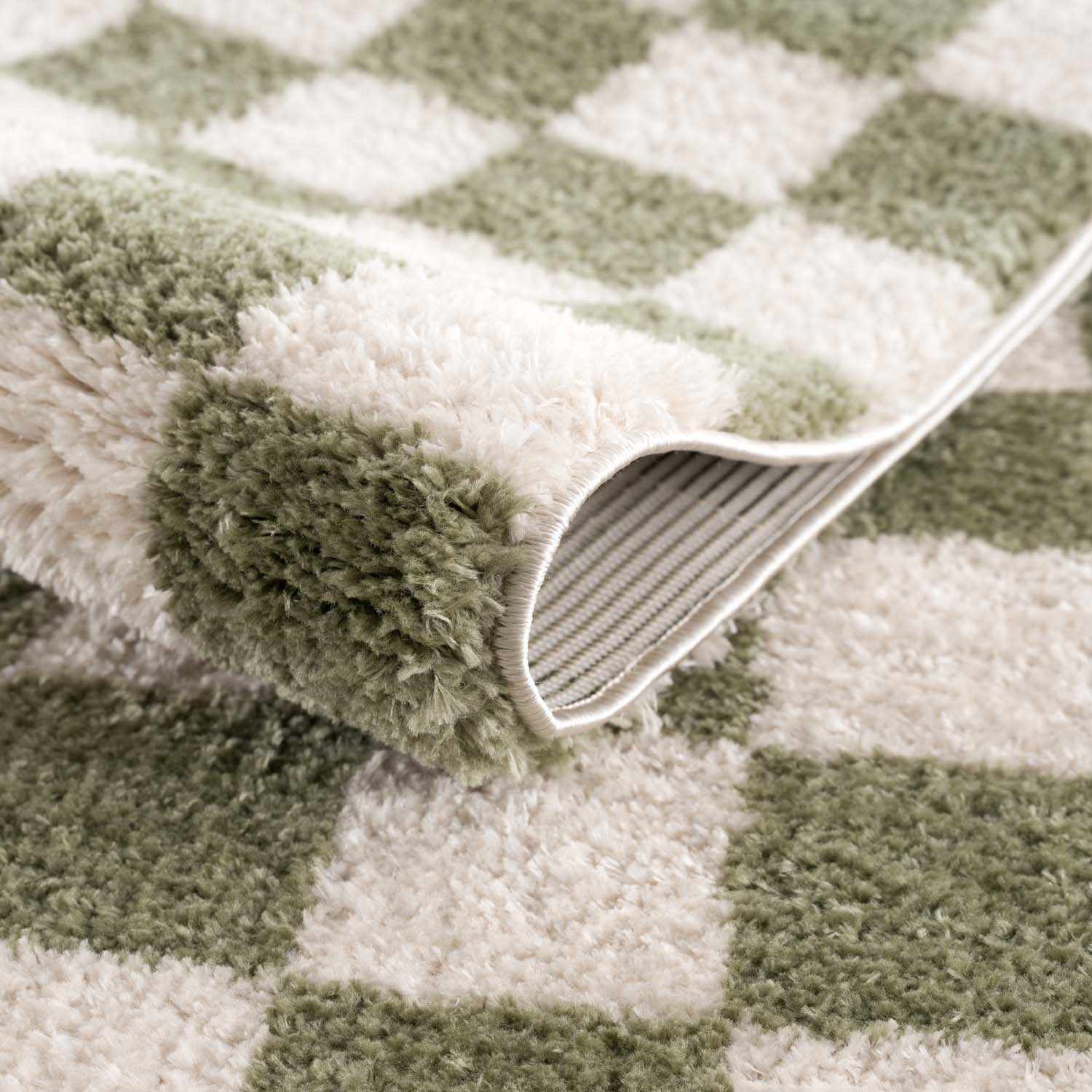 Close-up of the plush Canika Green Checkered Washable Rug, showing the green and off-white checkered pattern. Fold