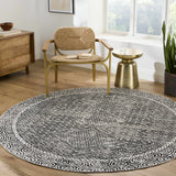 Living room scene with a round black and gray Consuelo Washable Area Rug under a chair and side table. Roomscene-Round
