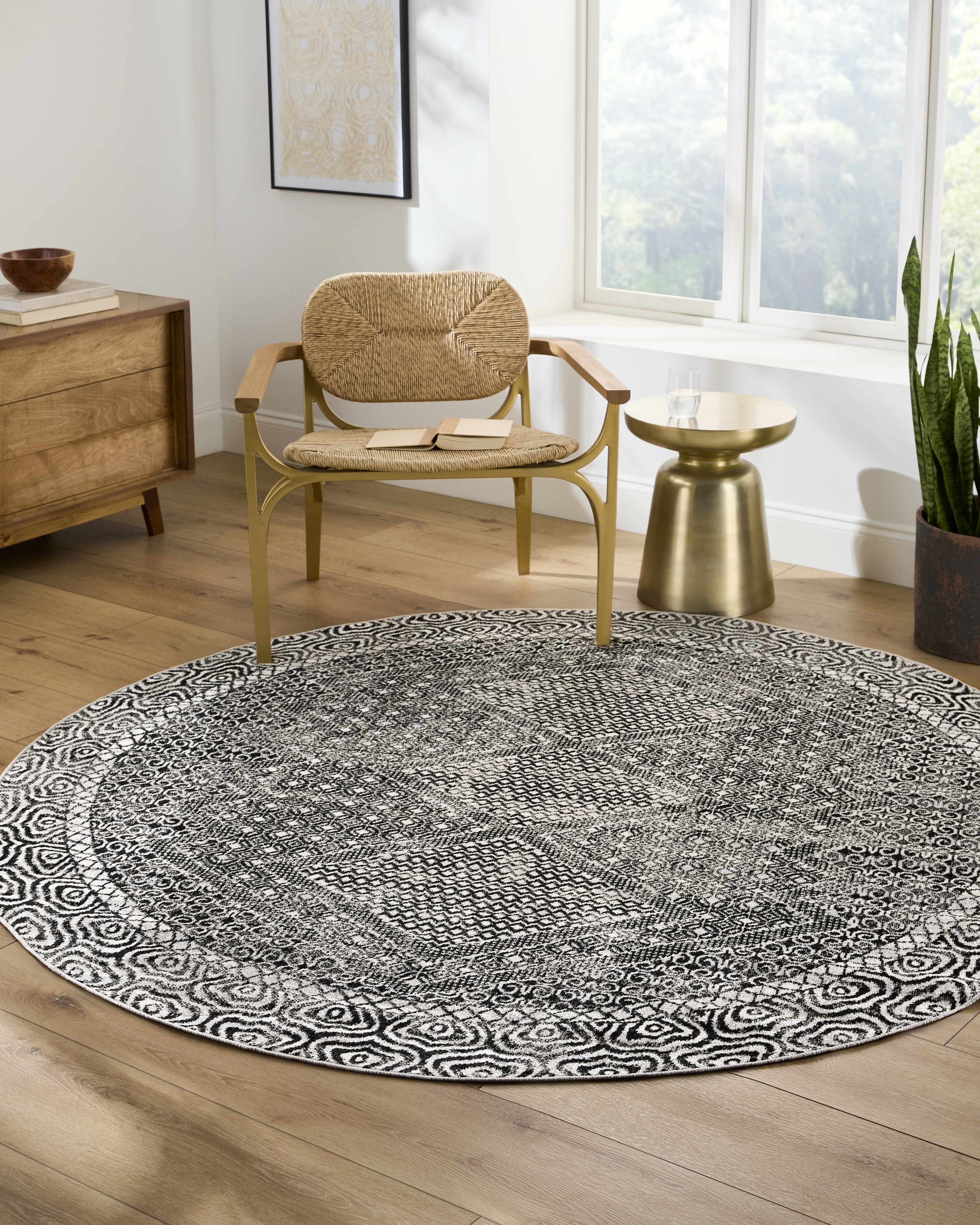 Living room scene with a round black and gray Consuelo Washable Area Rug under a chair and side table. Roomscene-Round