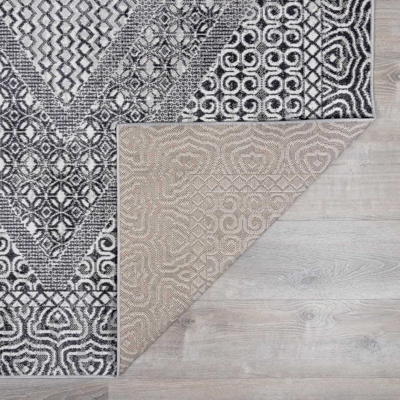 Close-up of the Consuelo Washable Area Rug showing its black, gray, and light gray oriental-inspired pattern and backing. Fold