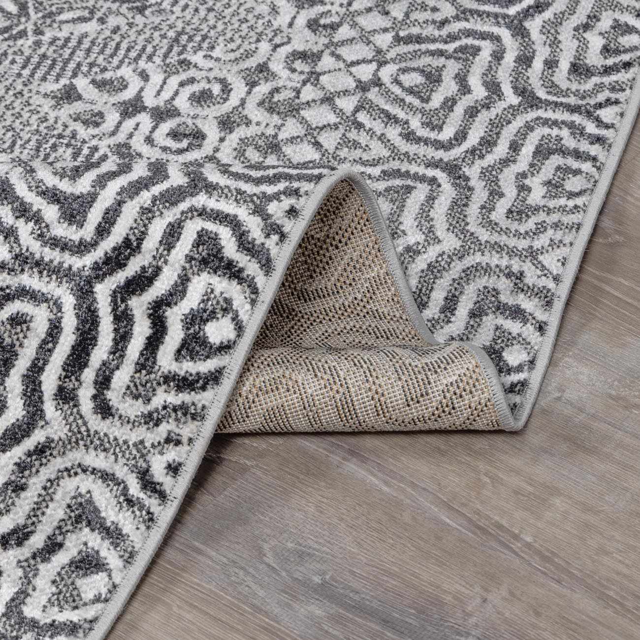 Close-up of the Consuelo Washable Area Rug, showcasing its black, gray, and light gray oriental pattern and machine-woven texture. Fold
