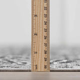 Close-up of the pile height of the gray and black Consuelo Washable Area Rug, shown with a ruler. Pile