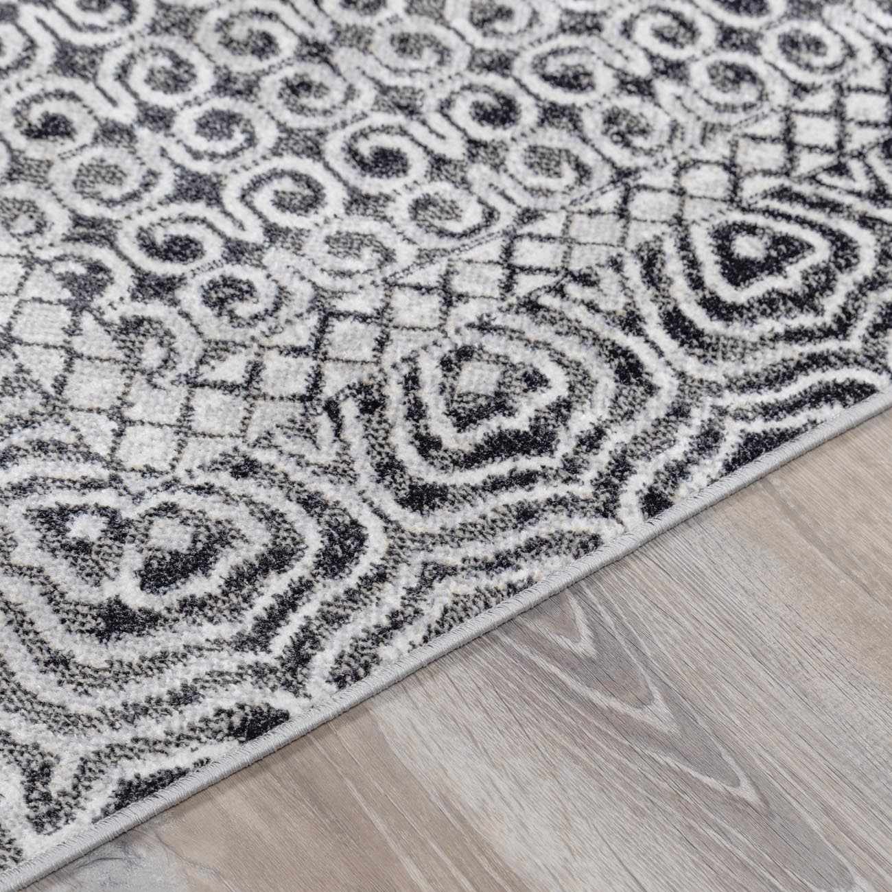 Close-up of the Consuelo Washable Area Rug, featuring a black and gray oriental-inspired pattern on a light gray background. Pile