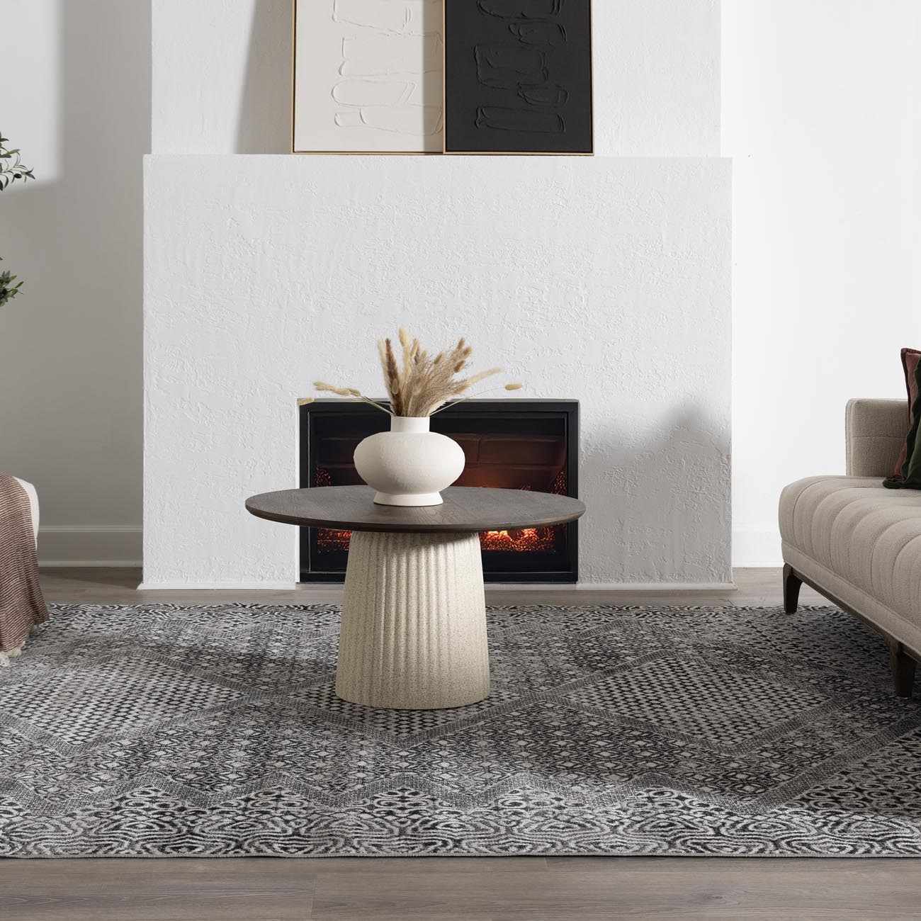 Living room scene with a gray patterned Consuelo Washable Area Rug, round coffee table, fireplace, and neutral sofa. Roomscene-Rectangle