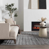 Living room scene with a gray and black Consuelo Washable Area Rug, beige sofa, fireplace, and round coffee table. Roomscene-Rectangle