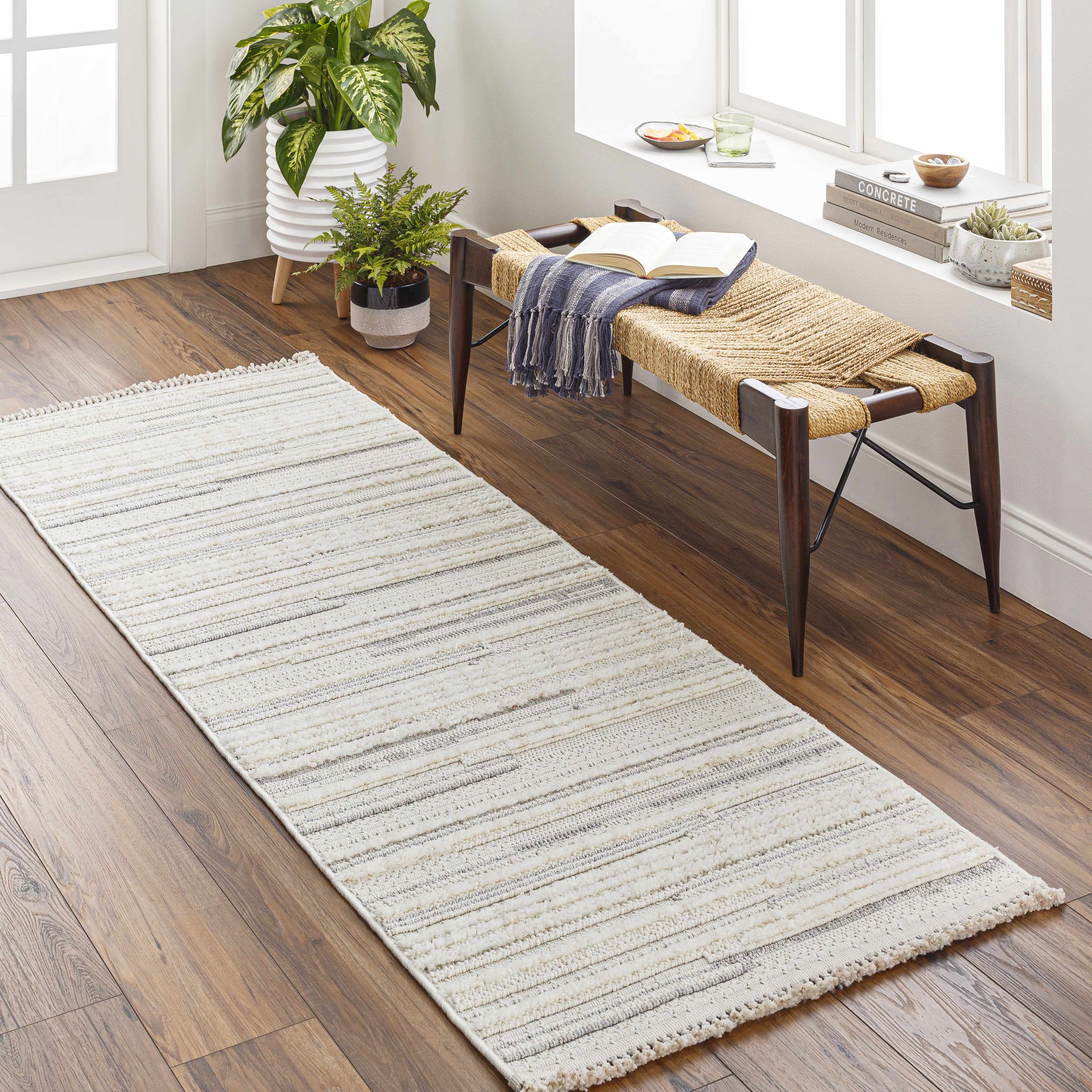 Entryway with cream and light gray striped Dishman Area Rug, wood floors, woven bench, and potted plants. Roomscene-Runner