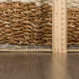 Close-up of Neyland Sage Green Area Rug showing the rug's texture, pattern, and braided trim next to a ruler and woven basket. Pile