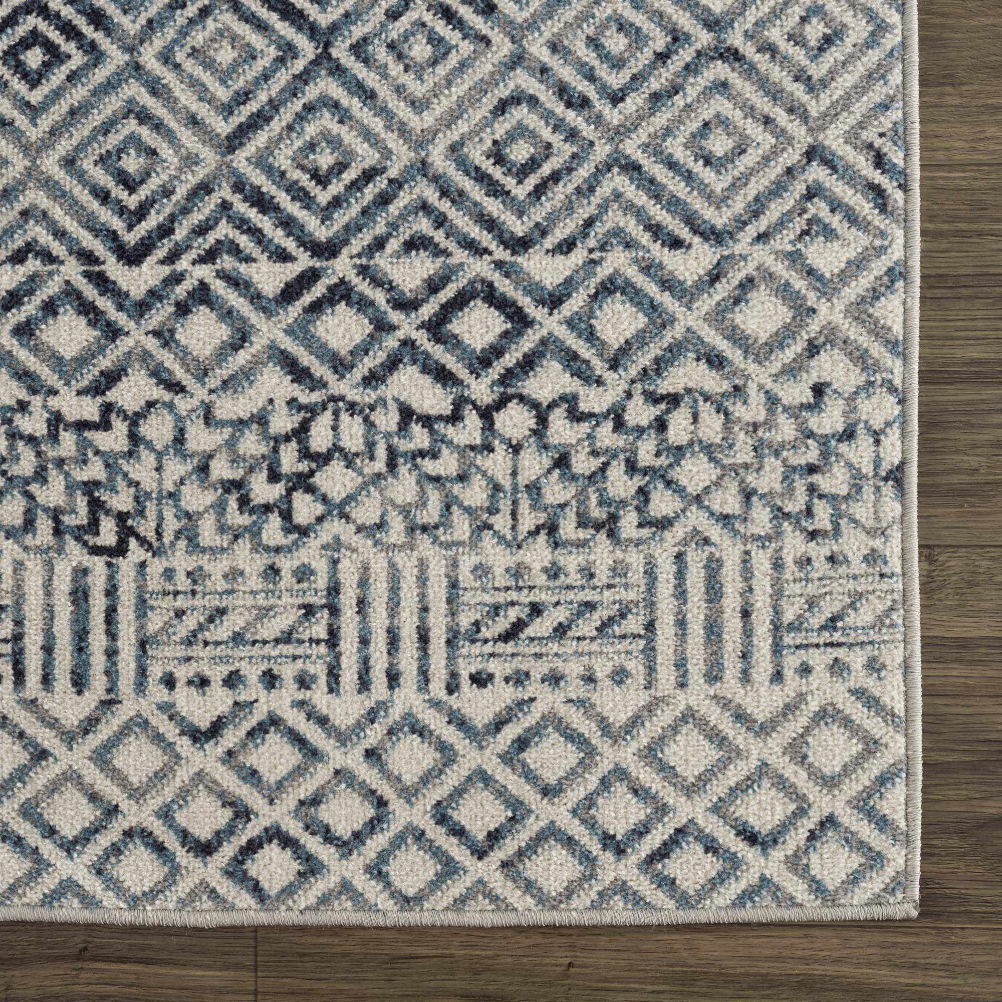 Close up of the Askeaton Washable Area Rug with blue, gray, and geometric patterns on a wood floor. Swatch