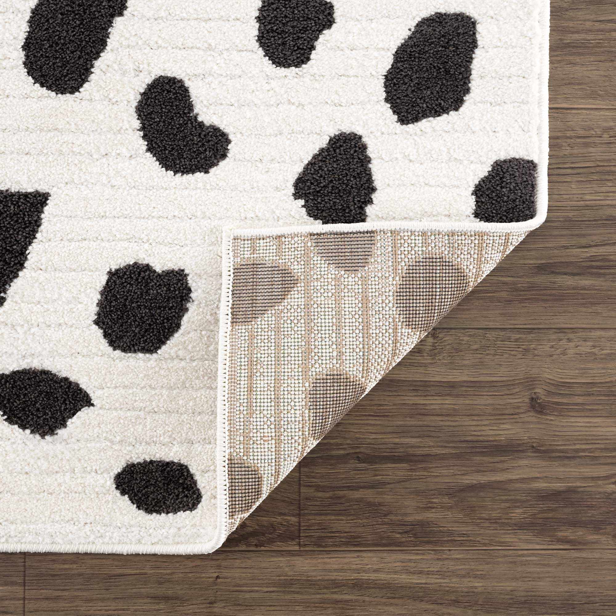 Close-up of the Tariffville Dalmatian Rug showing its black spots on an off-white shag pile and woven backing. Fold
