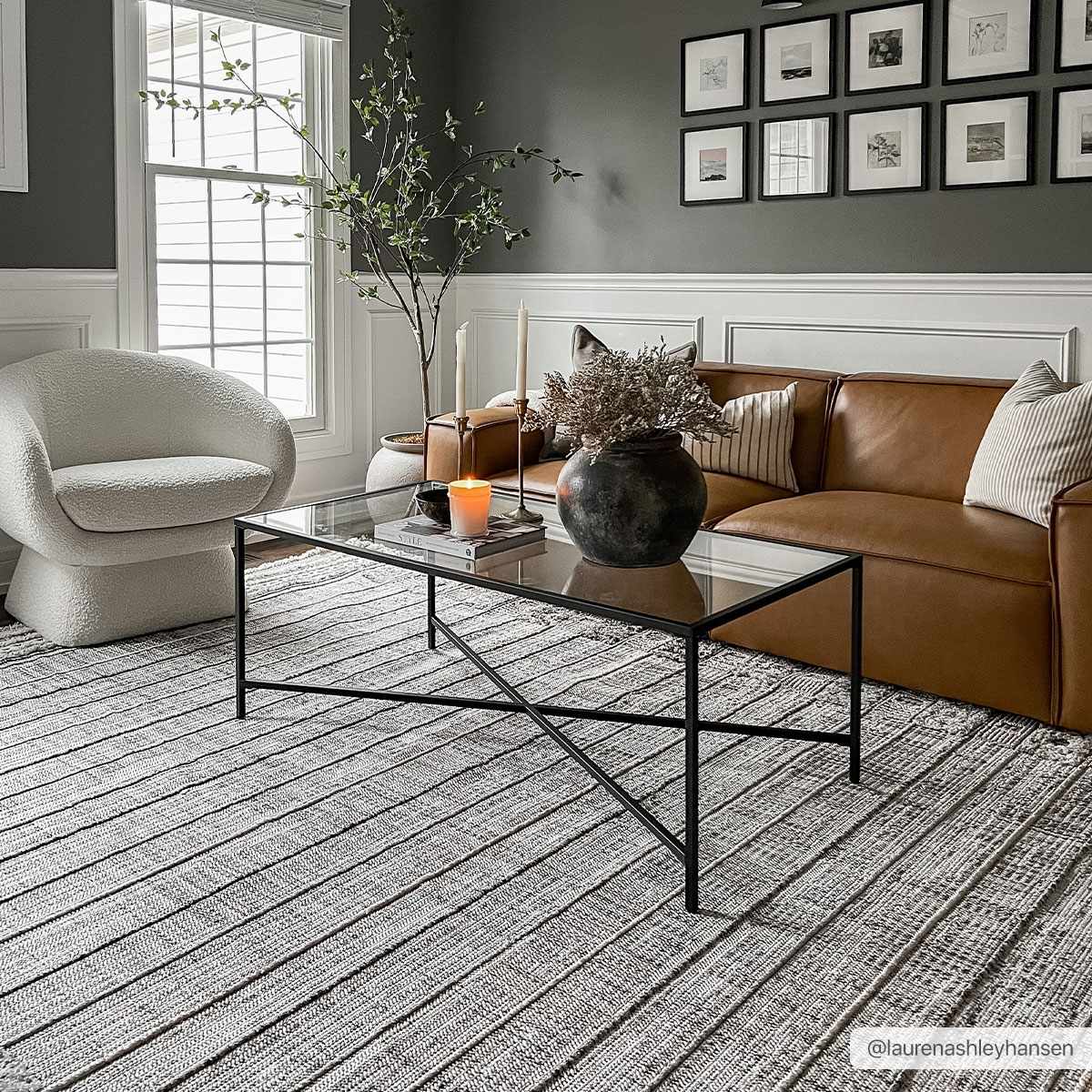Living room scene with a Naivasha Elegant High/Low Area Rug in charcoal and cream, leather sofa, and glass coffee table. Roomscene-Rectangle