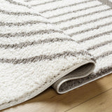 Close-up of the Jola Taupe Area Rug, showcasing its plush texture and geometric pattern in beige, bone, and gray tones. Fold