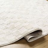 Close-up of the Keesa Checkered Area Rug. Ivory, off-white polyester rug with a subtle checkered pattern and soft, plush texture. Fold