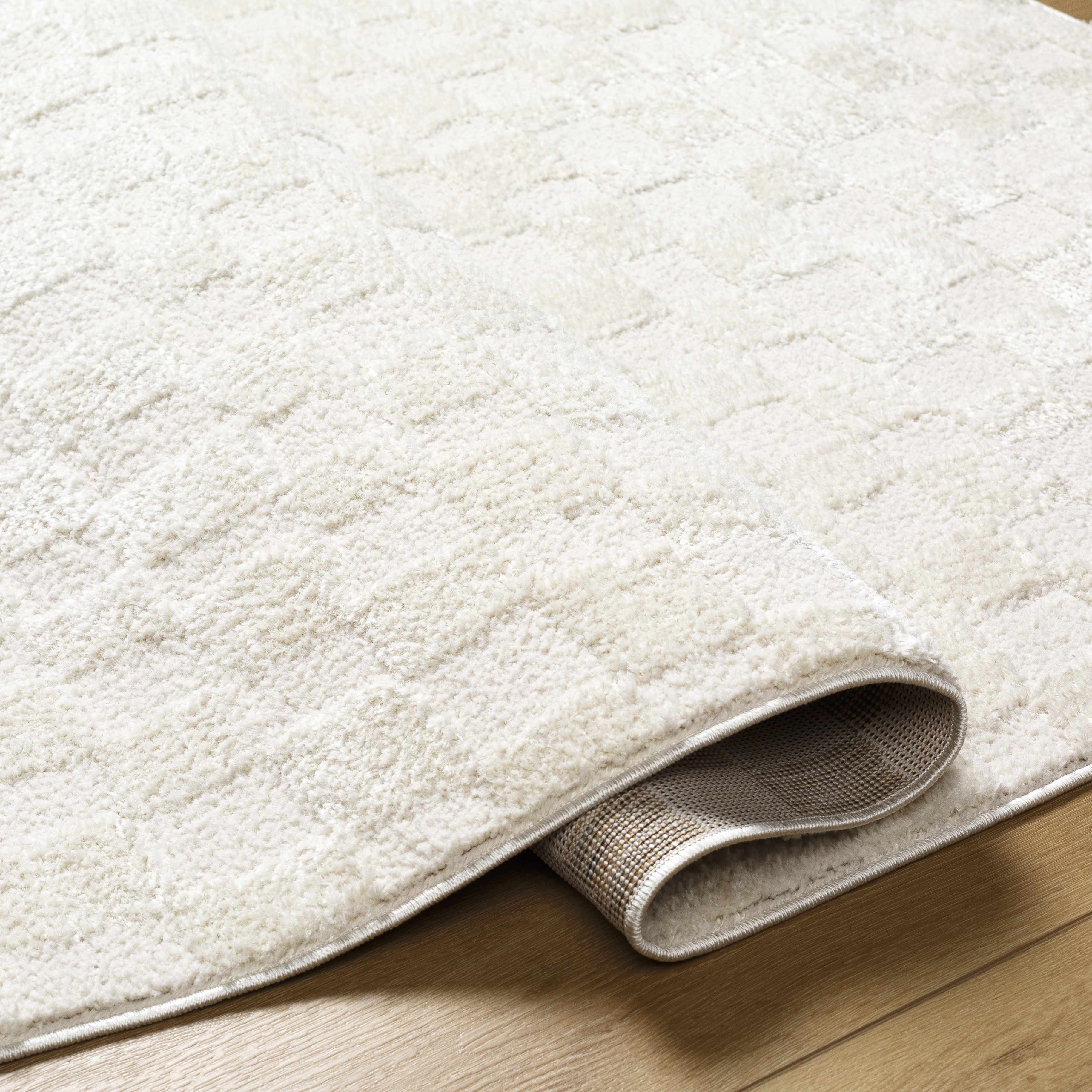 Close-up of the Keesa Checkered Area Rug. Ivory, off-white polyester rug with a subtle checkered pattern and soft, plush texture. Fold