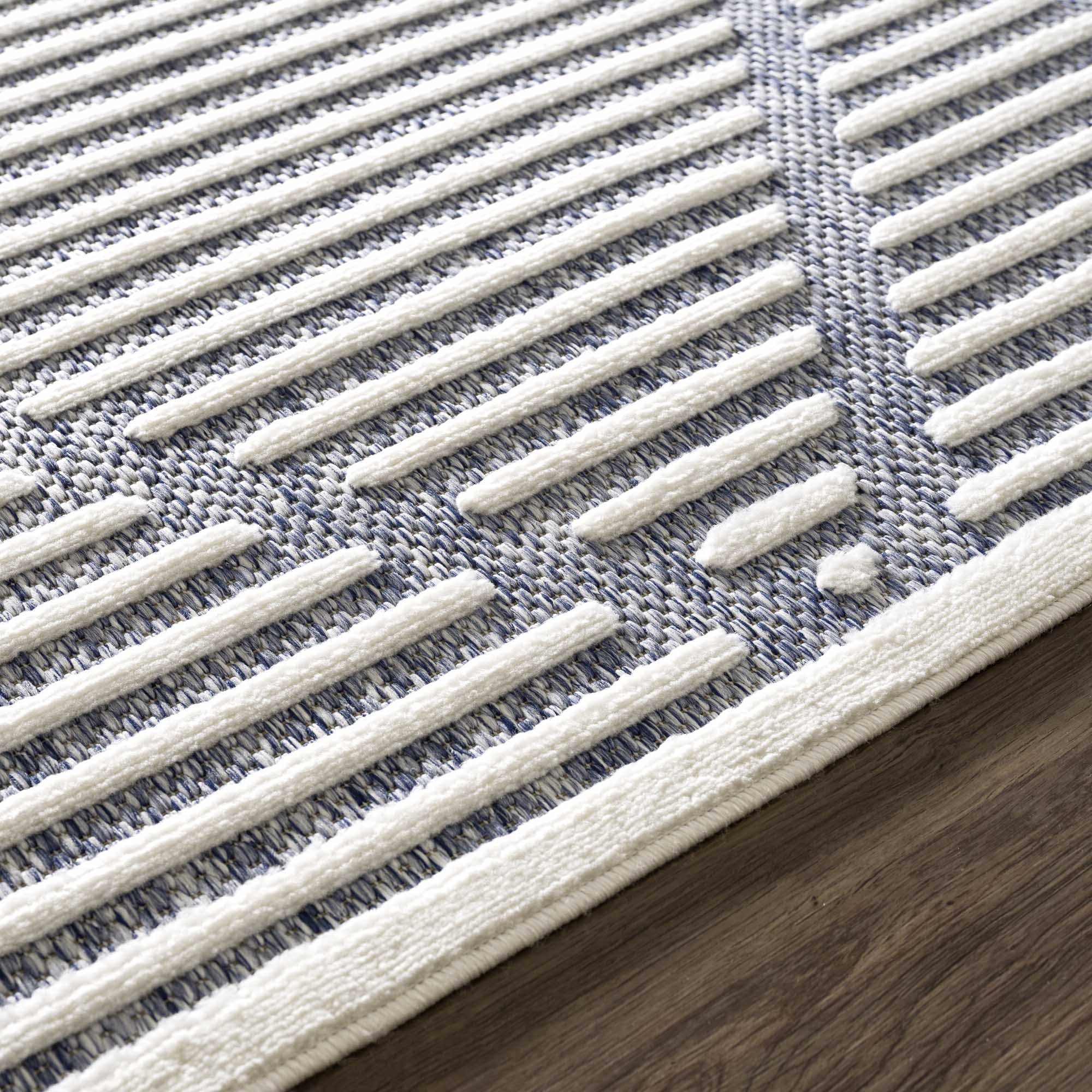 Close up of the Anah Blue Outdoor Rug showing the textured white stripes and blue woven background. Styleshot