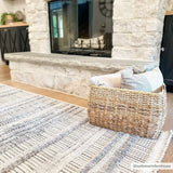Living room scene with a Silanga area rug in gray tones, styled with a stone fireplace and woven basket. Roomscene-Rectangle