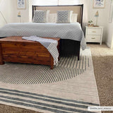 Bedroom scene with a Thad Medium Gray Washable Area Rug, wood chest, gray bedding, and white nightstand. Modern, cozy style. Roomscene-Rectangle