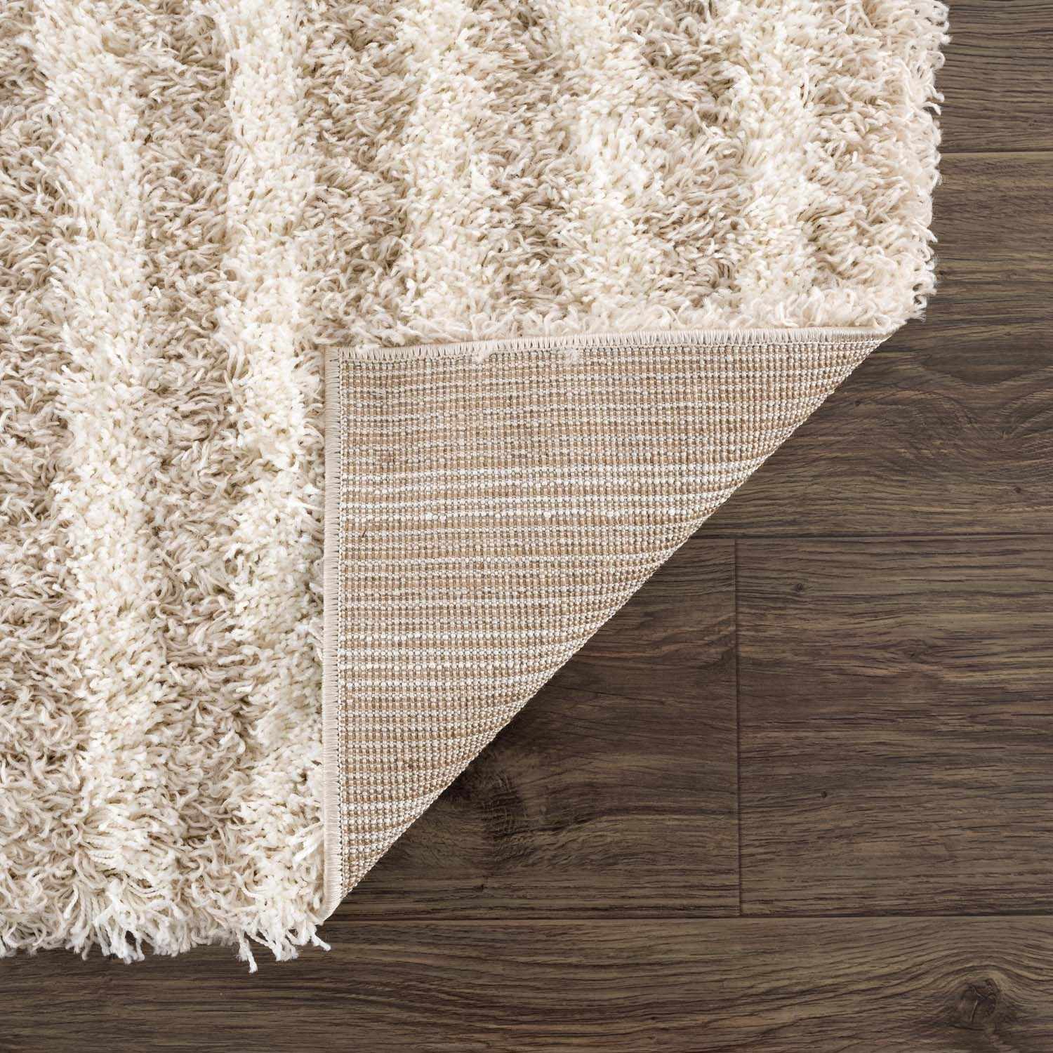 Close-up of the Emmly Shag Area Rug showing its white thatch, gray, and nutmeg colors, plus the rug's backing. Fold