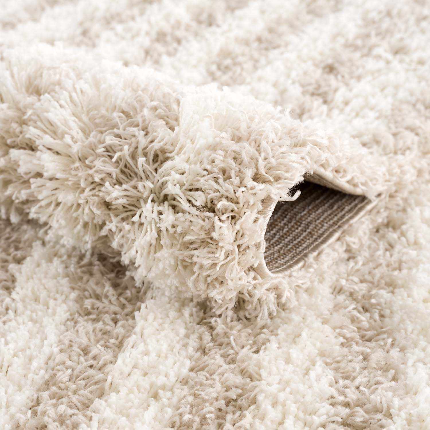 Close-up of the Emmly Shag Area Rug showing its plush, white thatch and light peach fibers, and machine-woven construction. Fold