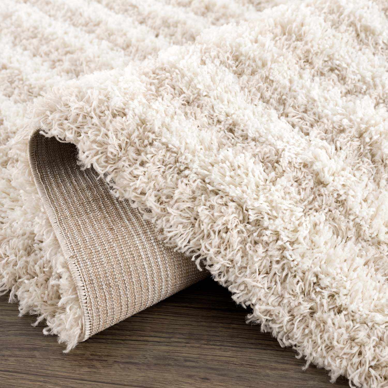 Close-up of the Emmly Shag Area Rug. Features a thick, plush white thatch pile with subtle gray and nutmeg tones. Fold