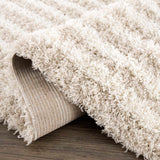 Close-up of the Emmly Shag Area Rug. Features a thick, plush white thatch pile with subtle gray and nutmeg tones. Fold
