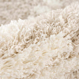 Close-up of the plush, soft texture of the Igor Shag Area Rug in light neutral tones. Fold