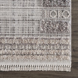 Close-up of the Naivasha Elegant High/Low Area Rug showing its charcoal, cream, and gray textured design and fringe. Swatch