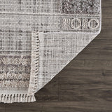 Close-up of Naivasha Elegant High/Low Area Rug showing charcoal, cream, and gray tones, plus fringe detail and rug backing. Fold