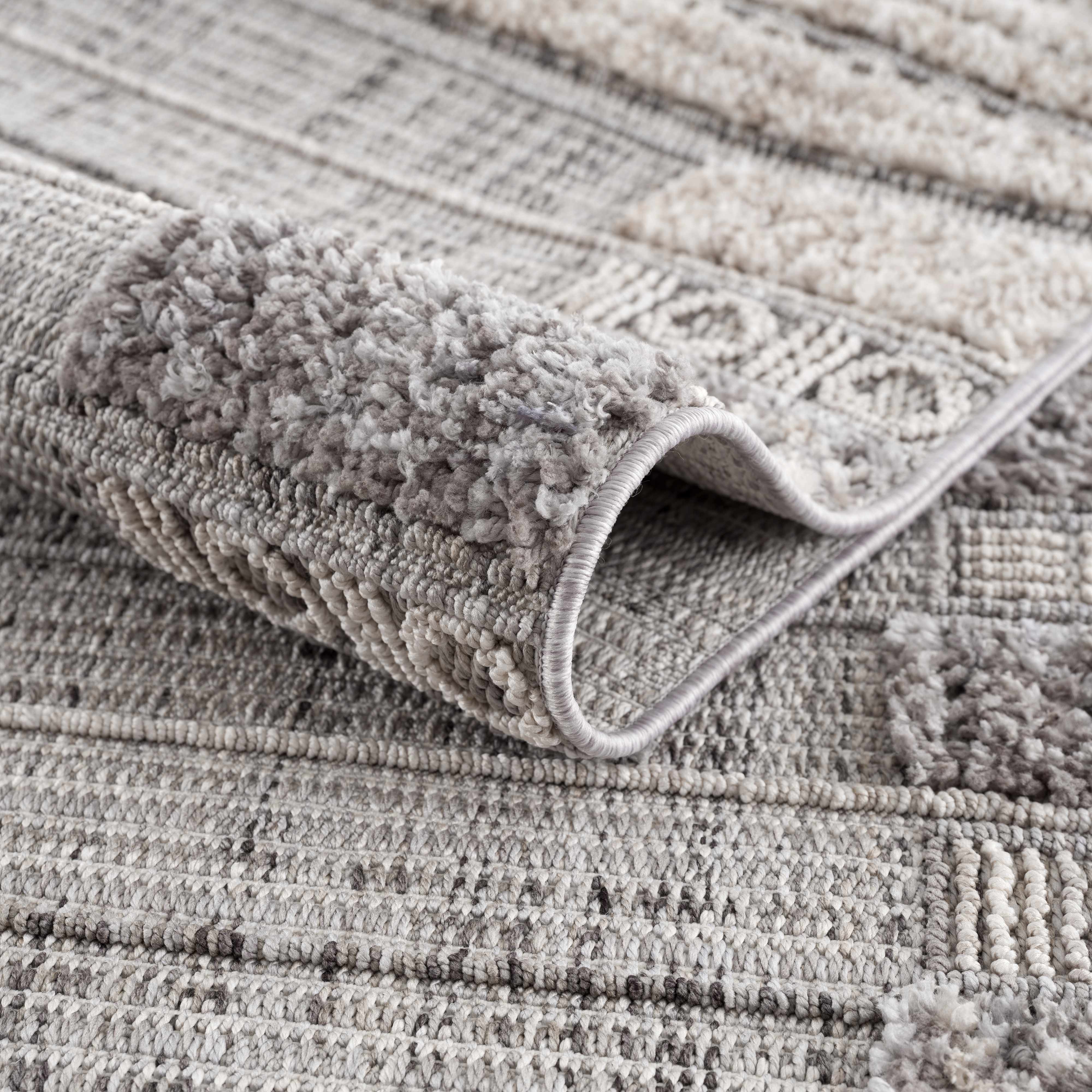 Close-up of Naivasha Elegant High/Low Area Rug. Charcoal, cream, and gray textured rug with a high-low pile design. Fold
