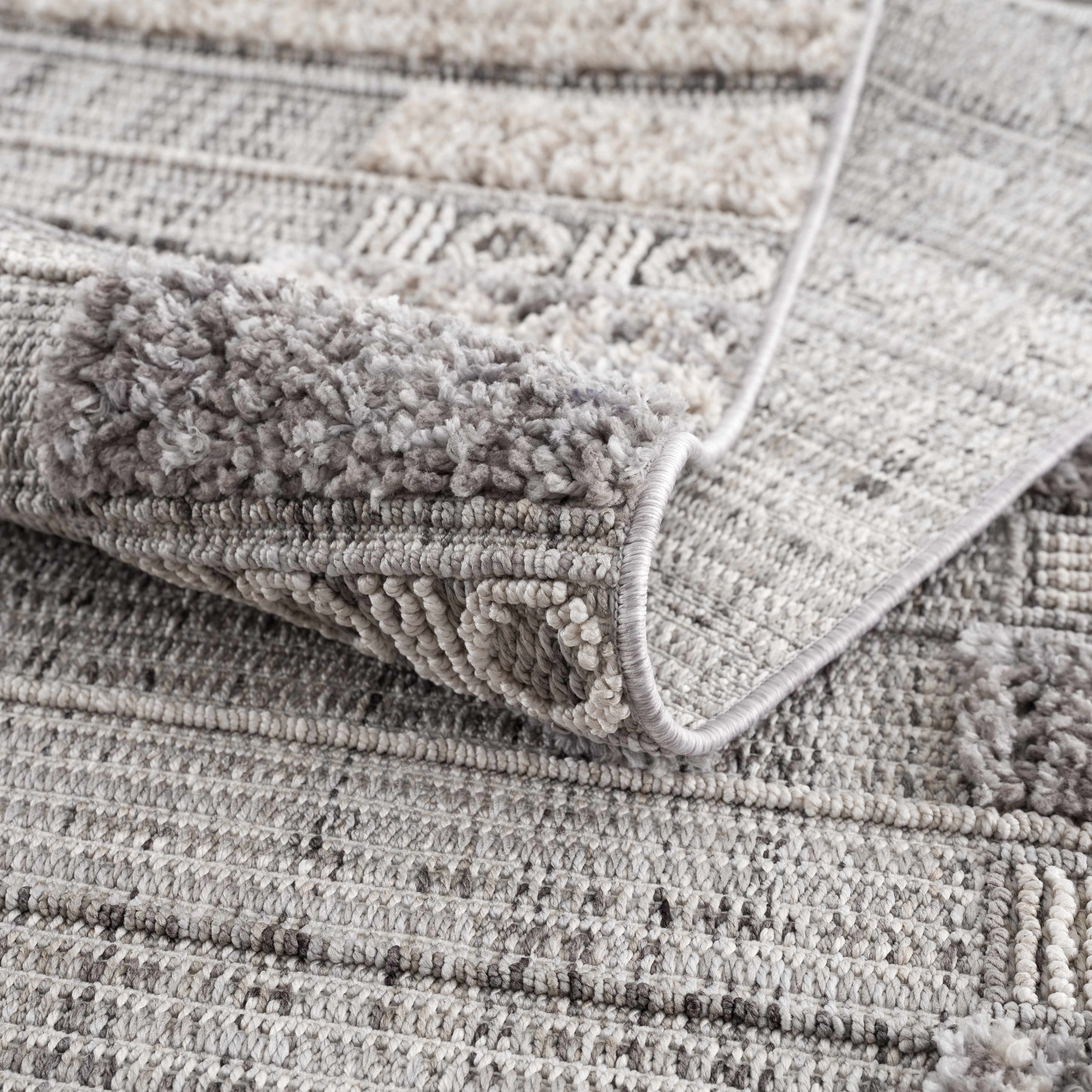 Close-up of the Naivasha Elegant High/Low Area Rug, showing its charcoal, cream, and gray textured pattern. Fold