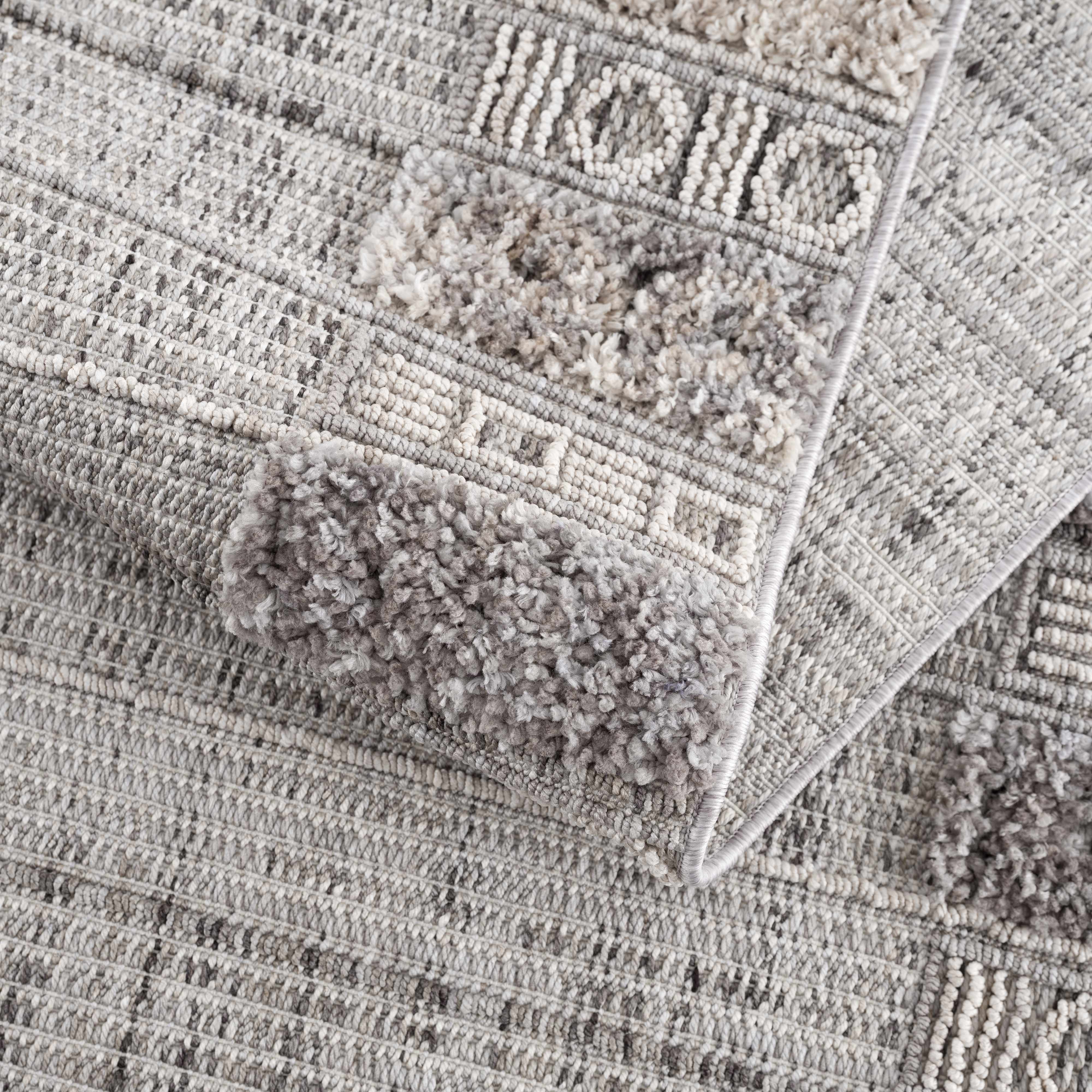 Close-up of the Naivasha Elegant High/Low Area Rug. Features a textured geometric pattern in charcoal, cream, and gray polyester. Fold