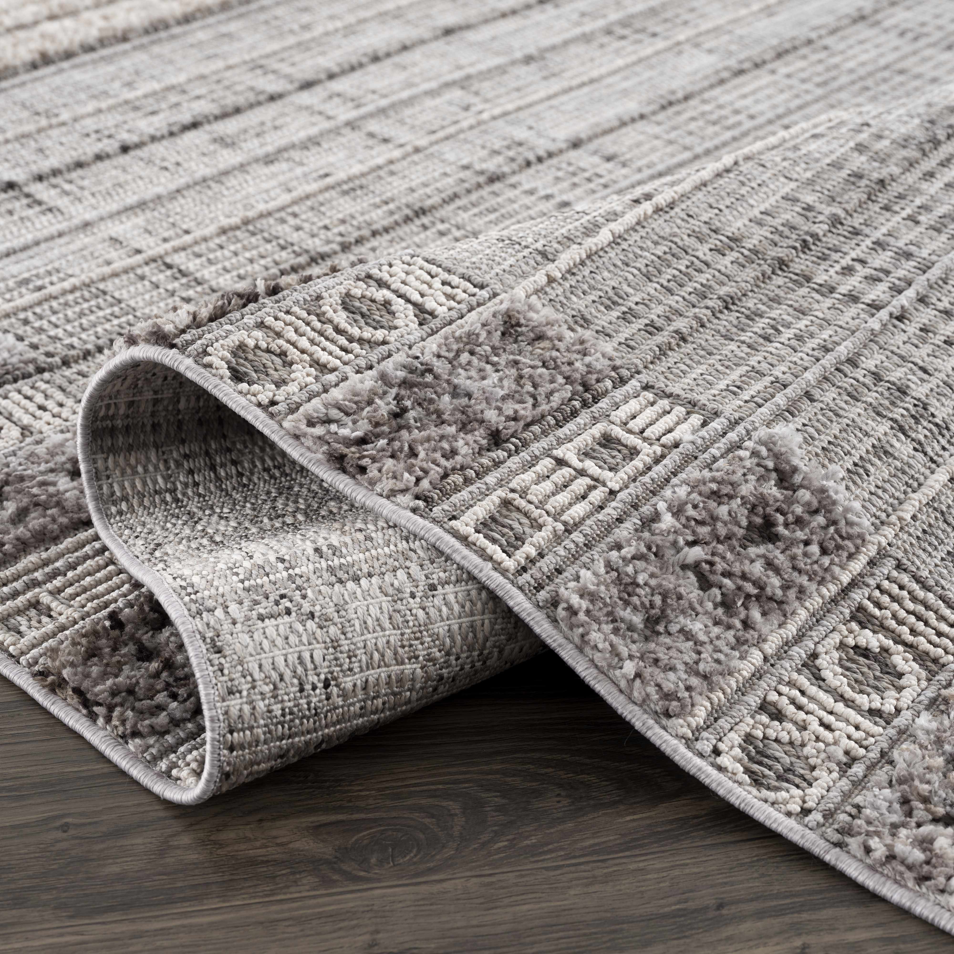 Close-up of the Naivasha Elegant High/Low Area Rug showing its charcoal, cream, and gray textured pattern. Fold