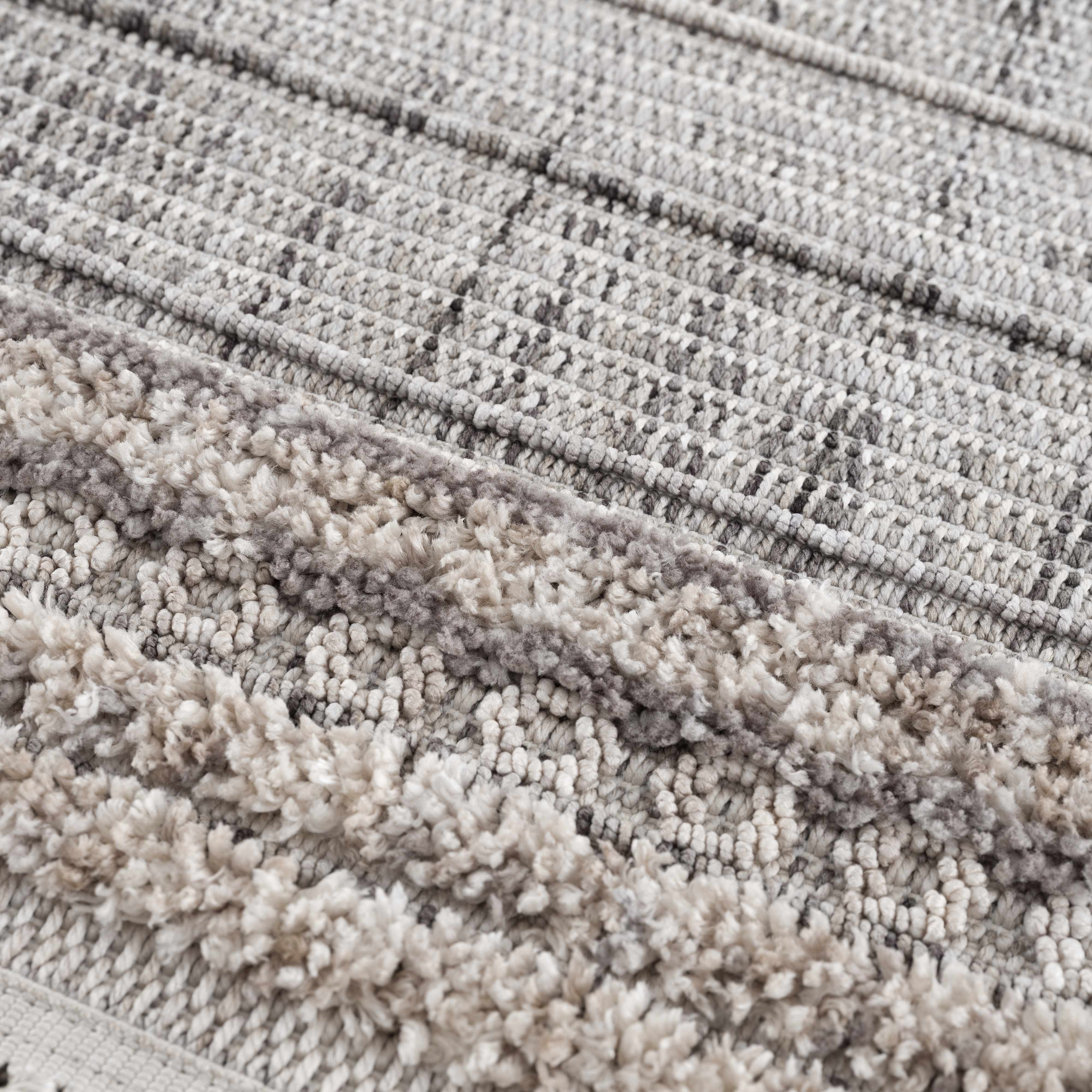Close-up of the Naivasha Elegant High/Low Area Rug. Features charcoal, cream, and gray tones with a textured, high-low pile. Texture