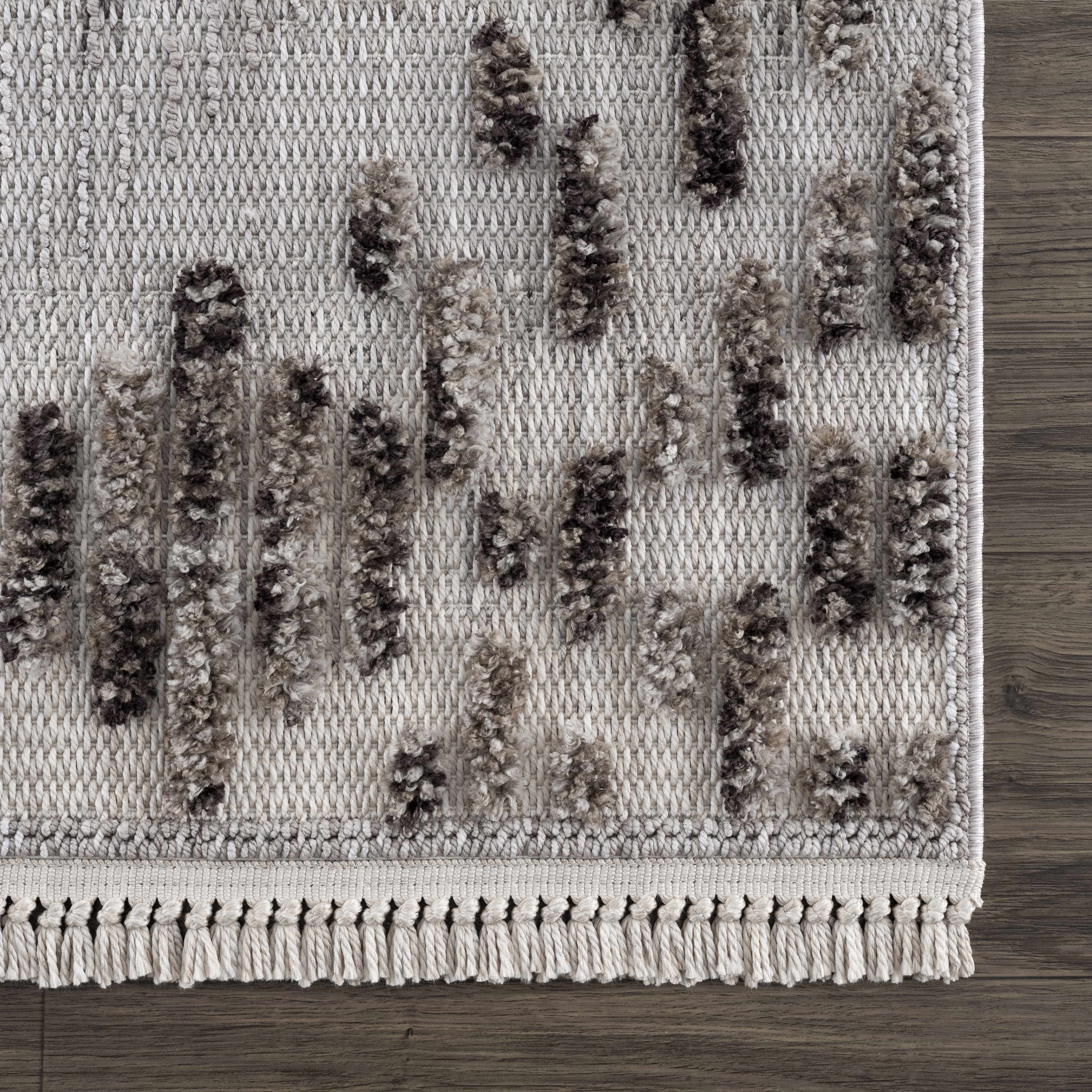 Close-up of the Cabarroguis Area Rug. Cream rug with charcoal geometric pattern and fringe detail. Swatch