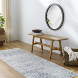 Entryway with a blue and gray geometric Askeaton Washable Area Rug, wood bench, round mirror, and woven basket. Roomscene-Runner