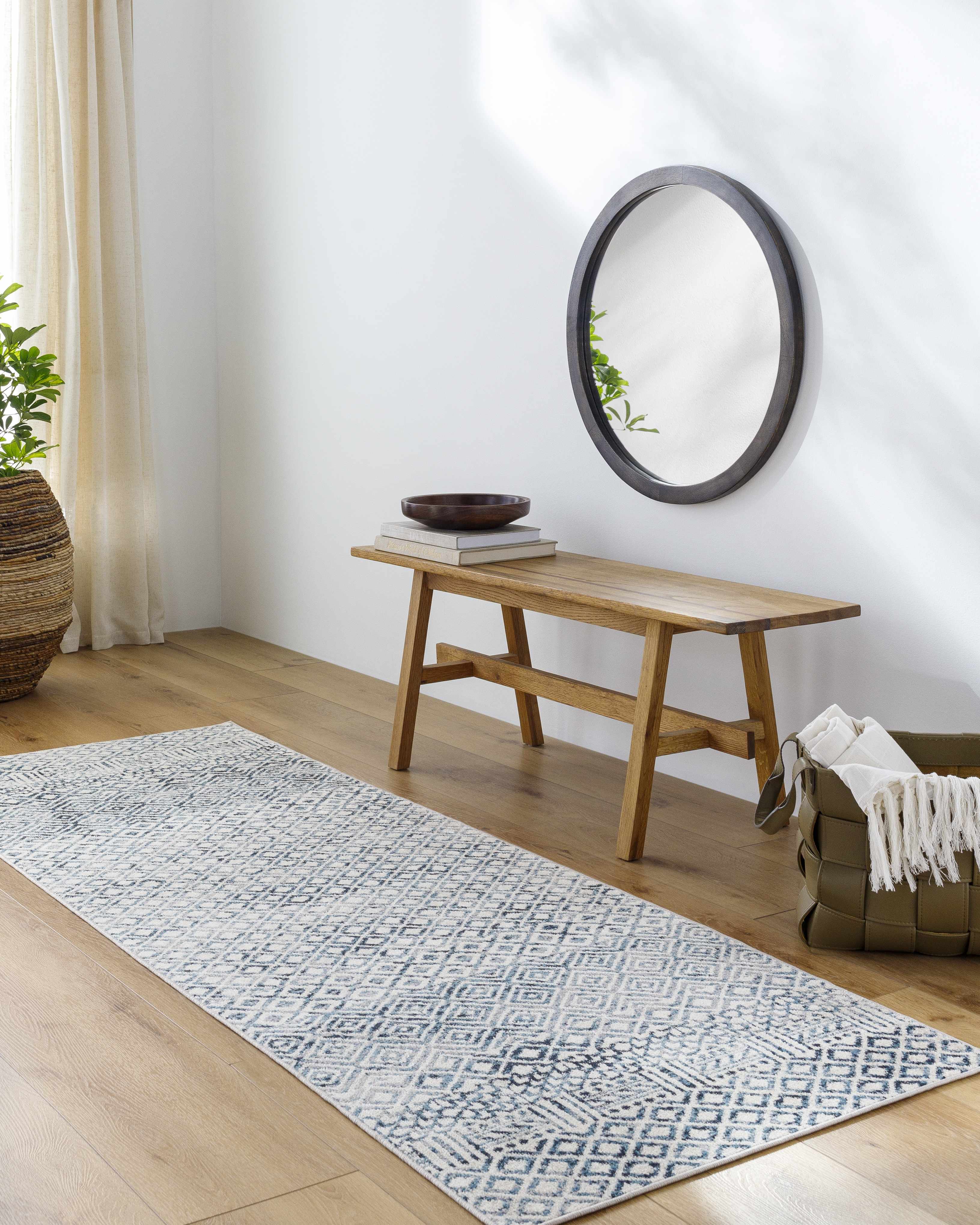 Entryway with a blue and gray geometric Askeaton Washable Area Rug, wood bench, round mirror, and woven basket. Roomscene-Runner