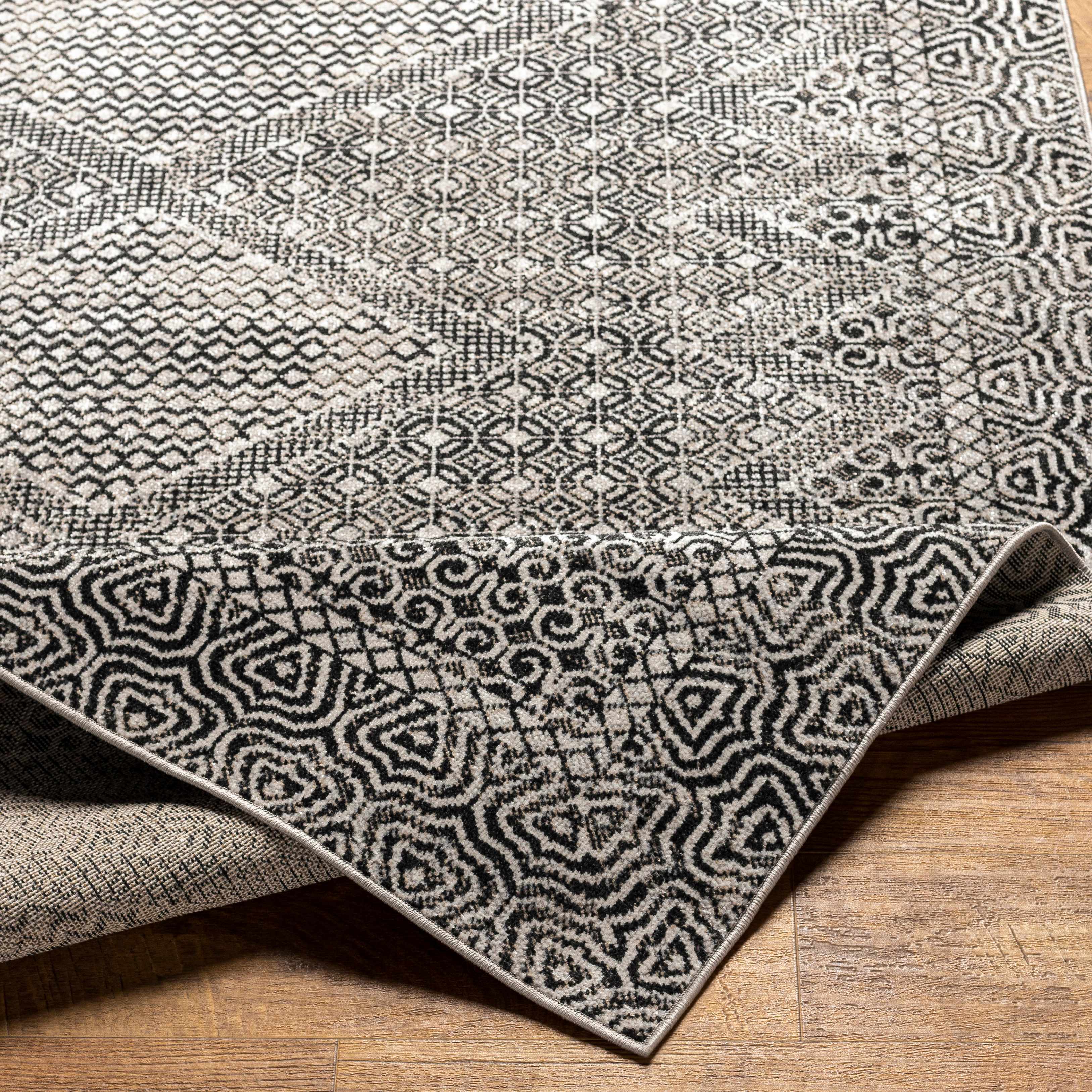 Close-up of the Consuelo Washable Area Rug, showcasing its black, gray, and light gray geometric pattern and machine-woven texture. Fold