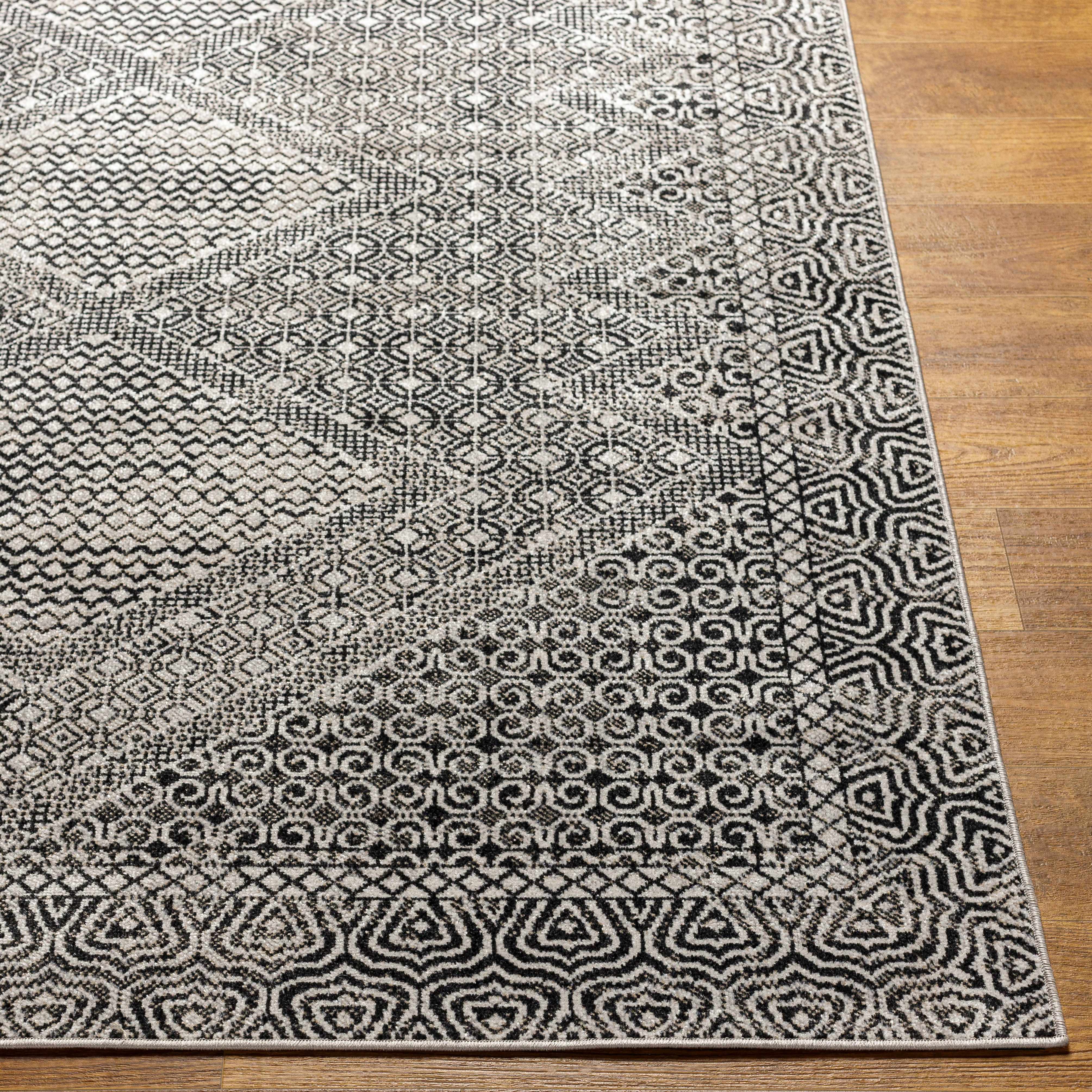 Close-up of the Consuelo Washable Area Rug. Black, gray, and light gray geometric patterns on a polyester rug. Front